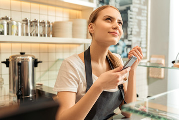 Wall Mural - Thoughtful waitress using phone in cafe