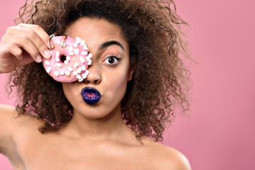 Wall Mural - Excited young african woman holding colorful doughnut