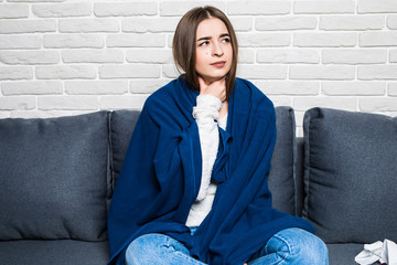 Terrible pain in her throat. young woman touching her neck while sitting on the couch at home.