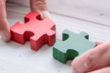 Two hands matching two pieces white jigsaw/puzzle whit one gap, over black wooden table background, symbol of problem solving.