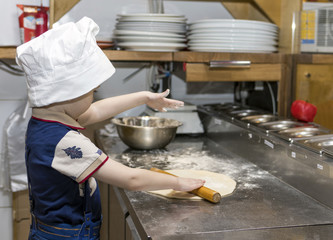 Child cook. A boy prepares pizza in the kitchen, makes dough from flour