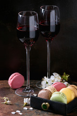 Two glasses of port wine with variety of colorful french sweet dessert macaron macaroons with different fillings served with spring flowers over dark texture background. Celebration concept