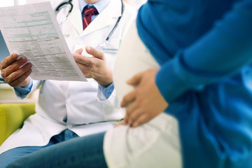 Close up of male doctor holding document while sitting with pregnant woman in clinic