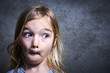 little child blond girl making faces with gray grunge wall background