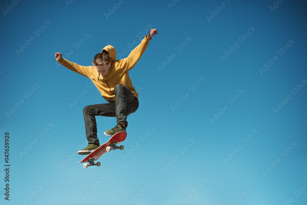 A teenager skateboarder does an ollie trick on background of blue sky gradient - obrazy, fototapety, plakaty 