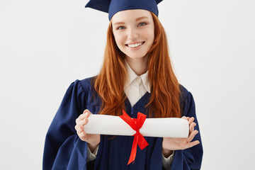 Close up portrait of happy foxy girl graduate in cap smiling holding diploma. Young redhead woman student future lawyer or engineer. White background.