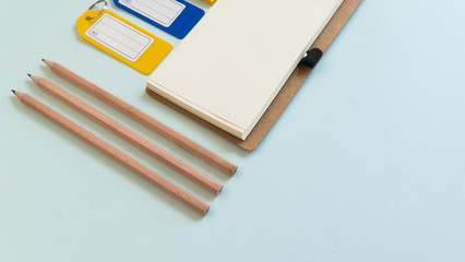 Notebook place on blue background with yellow post it, pencils and plastic tags