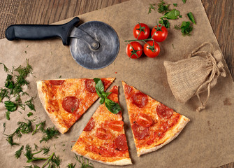 Flatlay or top view. Pepperoni pizza slices on craft bakers paper. Fresh tomatoes, parsey, circle knife and dill