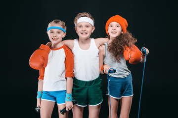 Wall Mural - Three smiling kids in sportswear posing with sport equipment and looking at camera