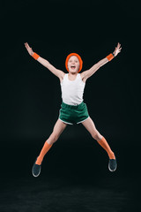 Wall Mural - Happy boy in sportswear jumping and looking at camera isolated on black