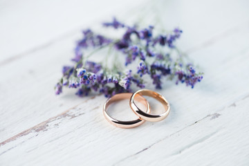 Close-up view of golden wedding rings and beautiful small blue flowers on wooden tabletop
