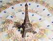 Eiffel Tower souvenir surrounded by vacation money. A lot of euro bills. Travel budget concept.