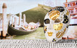 Mask from Venice with a gondola moored by Rialto Bridge. Golden and decorative souvenir and a traditional Venetian boat in the canal in the blurred background. Summer holiday and travel concept.