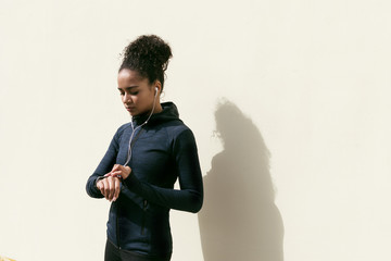 Wall Mural - young woman checking activity tracker on her wrist during outdoor exercise, standing at wall