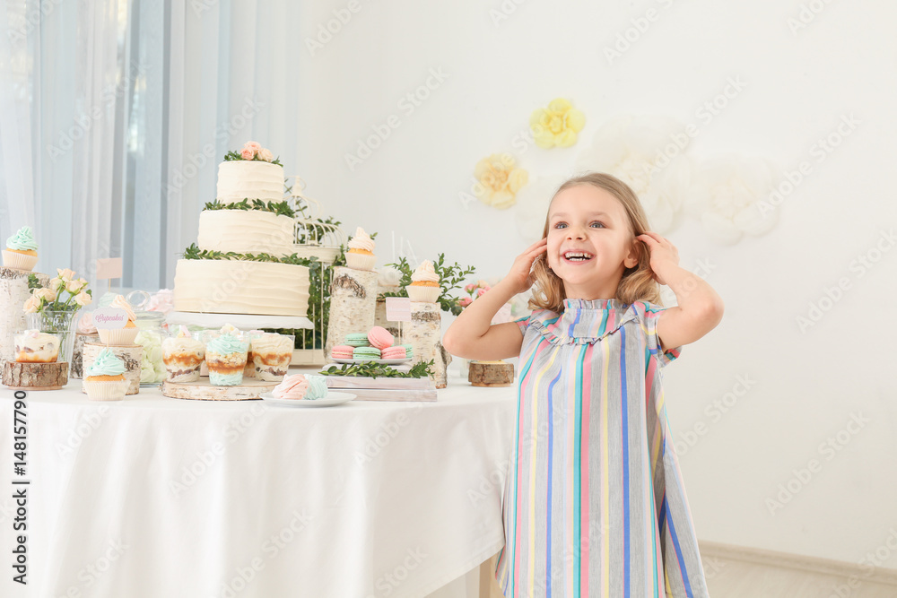Cute girl near table with sweets served for party