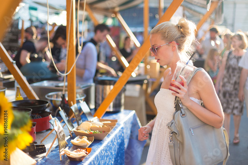 Cuadros en Lienzo Beautiful blonde caucasian lady wearing white summer dress buying freshly prepared meal at a local street food festival