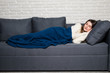 © F8  \ Suport Ukraine - Young woman lying on sofa at home, sleeping covered with warm blanket at home