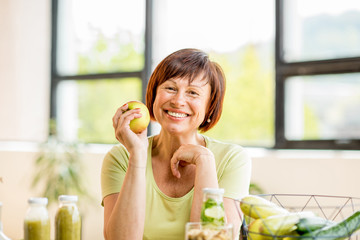 Portrait of a beautiful older woman with green healthy food on the table indoors on the window background