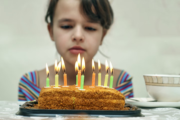 sad teen girl looking at birthday cake with burning candles