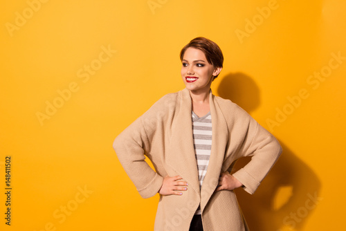 Fotografía Stylish young beautiful girl in fashionable beige cardigan is standing on bright yellow background
