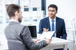 © LIGHTFIELD STUDIOS - Smiling man in suit and eyeglasses gesturing and looking at businessman with clipboard, business concept