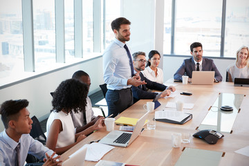 Wall Mural - Businessman Stands To Address Meeting Around Board Table