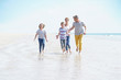 © goodluz - Happy family of four walking on sandy beach