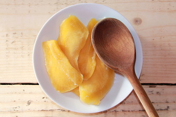 Dried mangoes on a White plate with a wooden spoon