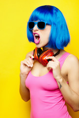 Wall Mural - Beautiful young sexy girl dj in blue wig blue sunglasses and pink bathing suit having fun and listening to music in red headphones on yellow background