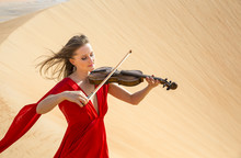 Woman In A Red Dress Playing Violin In A Desert In Abu Dhabi