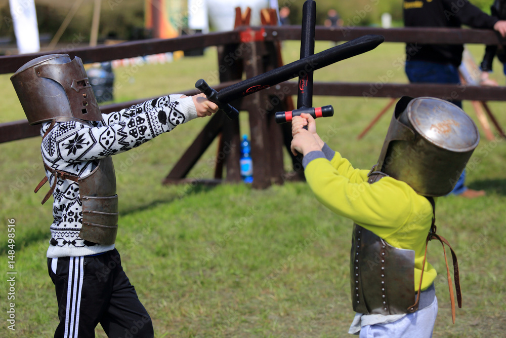 Dwóch chłopców w zbrojach rycerskich walczą na miecze. - obrazy, fototapety, plakaty 