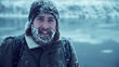 Young man with beard and long brown hair with snowbound hat, jacket and face smiling at camera