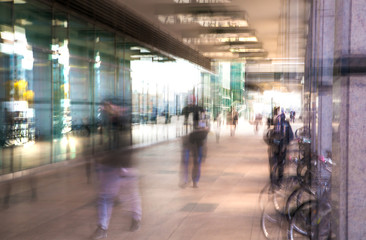 Poster - Abstract, blurred image of people walking via long tunnel with light at the background.
