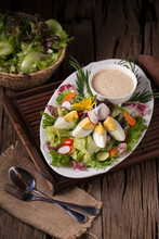 Shot Of Green Salad With Radish And Hard-boiled Egg On White Plate With Fork And Napkin