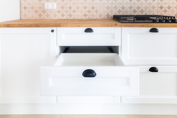 Opened kitchen drawer, kitchen in a traditional style with wooden white fronts, black handles and wooden countertop 