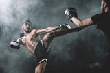 side view of concentrated muay thai fighter practicing kick isolated on black, fight club concept