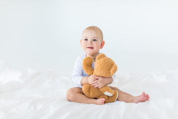 Portrait of adorable small baby boy with teddy bear playing on bed, 1 year old baby concept