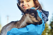 Smiling schoolgirl holding little goat in her hands