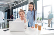© LIGHTFIELD STUDIOS - Smiling young businesswomen using laptop and talking at workplace
