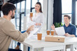© LIGHTFIELD STUDIOS - Professional young businesspeople drinking coffee from paper cups and discussing papers in small business office