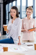 © LIGHTFIELD STUDIOS - young businesswomen with cup of coffee and tablet at modern workplace
