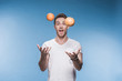 Smiling young man juggling with fruits isolated on blue