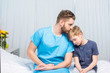 © LIGHTFIELD STUDIOS - Sick father and upset son sitting together on hospital bed, dad and son in hospital