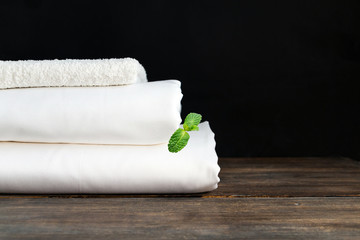 Stack of white clean new bed sheets on wooden desk against black background. Copy space. Concept of comfortable and stylish rest and dream. Mint leaves as freshness concept.