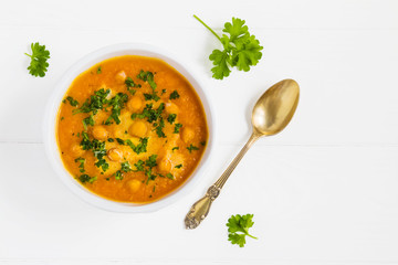 Carrot cream soup with chickpeas in white bowl on the wooden table, top view.