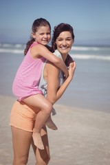 Wall Mural - Portrait of smiling mother piggybacking daughter at beach