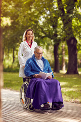 Wall Mural - smiling nurse pushing elderly man in wheelchair while reading book .