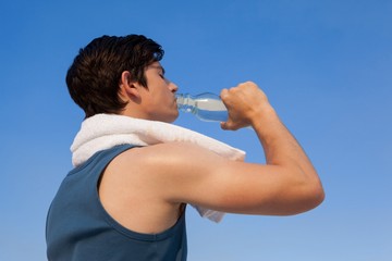 Canvas Print - Man drinking water from bottle against blue sky