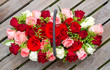  Rosengesteck mit roten, rosafarbenen und weißen Rosen auf einem Holztisch