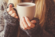 Young woman's hands holding a mug and warming with hot coffee.